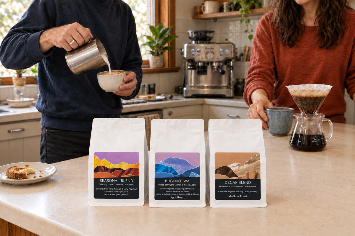 Three Monastery Coffee bags on a kitchen bench while one partner pours milk into a flat white and the other holds a mug beside a pour-over.
