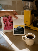 Coffee bag held beside a home batch brewer in warm morning light