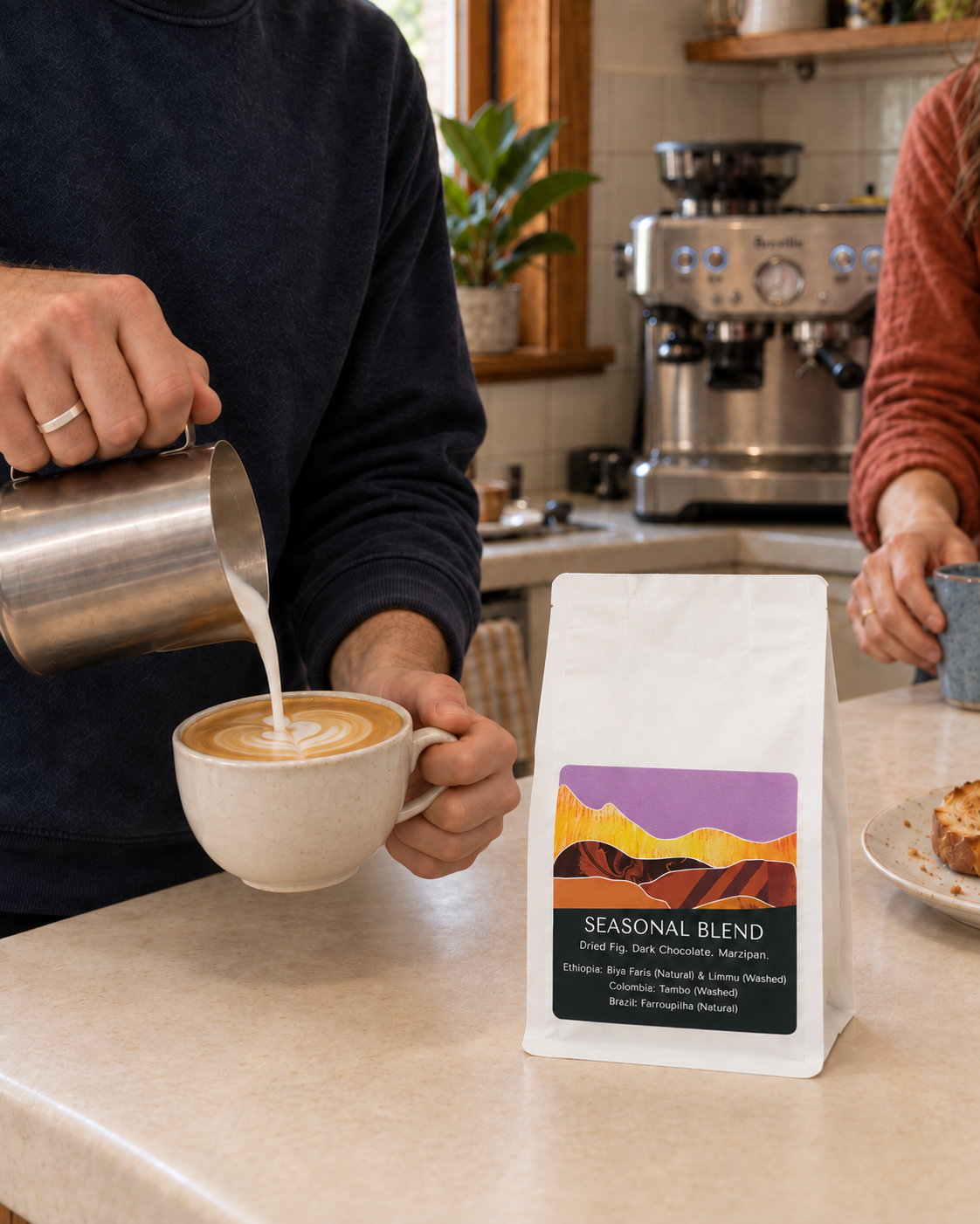 Monastery Seasonal Blend coffee bag beside a cream cup as milk is poured into a flat white in an Adelaide kitchen.
